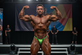 Thefreeway DN109 pistachio green laminated competition bodybuilding posing trunks worn on stage by a male bodybuilder in a front double biceps pose