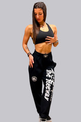 Unisex black bodybuilding training pants by Thefreeway Sportswear worn by a female model, front view with white leg logo